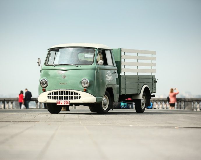 Vintage green truck parked in an open area with people in the background.