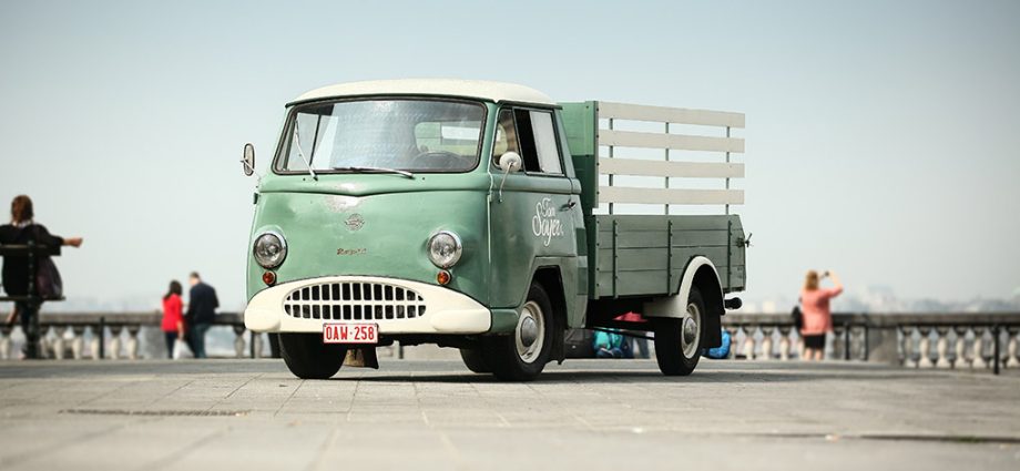 Vintage green truck parked in an open area with people in the background.